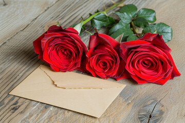 Close-up of three vibrant red roses alongside a blank love note, set on a rustic wooden surface