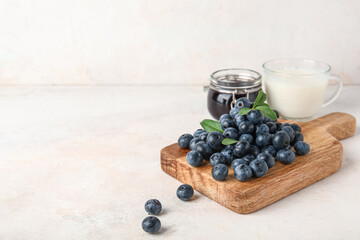 Wooden board with fresh blueberries and jar of jam on white background