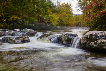 Serene Autumn River Flow with Silky Water Effect and Lush Foliage