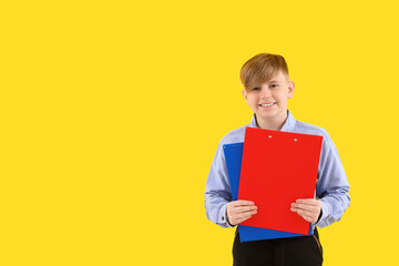 Little schoolboy in stylish uniform with notebooks on yellow background