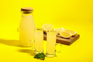 Shots and bottle of tasty Limoncello on yellow background