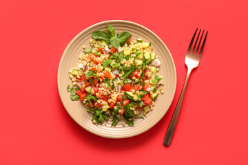Plate with delicious tabbouleh salad and fork on red background