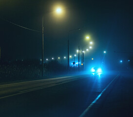 The headlights of an oncoming car tear through the darkness of the city at night