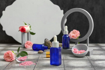 Bottle of cosmetic oil with rose extract and flowers on grey tile table