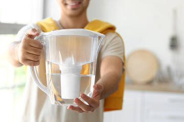 Young man with water filter jug in kitchen