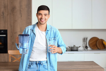 Young man with filter jug and glass of fresh water in kitchen