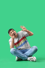 Afraid young man sitting on green background