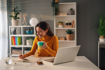 Portrait of a female student working on her project at home while drinking tea