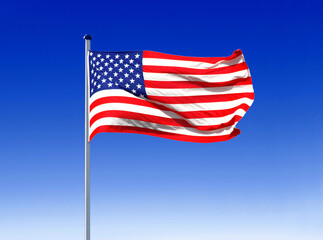 the national flag of the USA flies in the wind on a flagpole with a blue sky as a backdrop