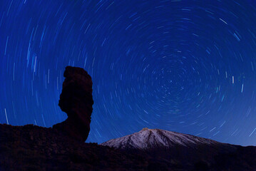 the Roque Cinchado at night with circling stars in the clear night sky and the summit of Pico de...