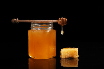 Jar of sweet honey and comb on black background