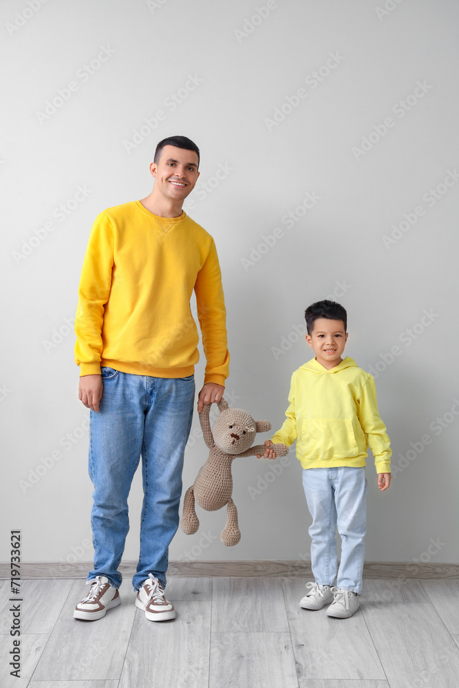 Canvas Prints young man and his little son with toy bear near light wall