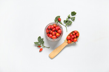 Jar and wooden spoon with fresh rose hip berries on white background