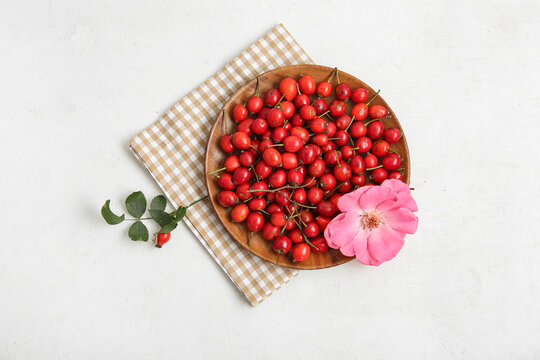 Wooden plate with fresh rose hip berries and flower on white background