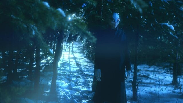 Creepy alien standing in snowy forest during the night and staring in the dark. Ufo light beams shining through trees from behind