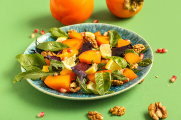 Plate of delicious salad with persimmon, pomegranate seeds and walnut on green background