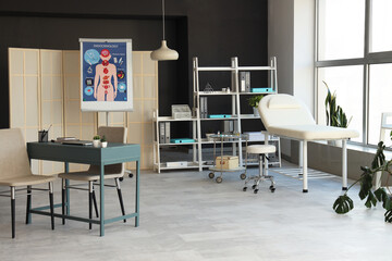 Interior of modern medical office with workplace, couch and shelf unit