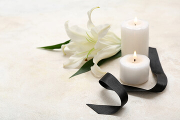 Fototapeta na wymiar Burning candles, black funeral ribbon and lily flower on light background