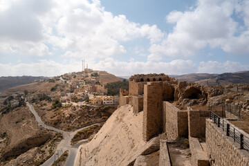 Al Kerak Castle walls in Jordan, overlooking a small village in the hot Middle Eastern autumn with cloudy sky and countryside hills. Medieval built occupied by crusaders