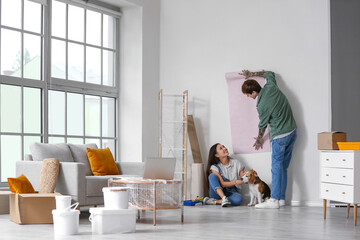 Young couple with Beagle dog wallpapering during repair in their new house - obrazy, fototapety, plakaty
