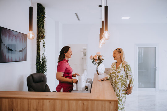 A beautiful blonde woman conversing with the dental clinic receptionist, scheduling an appointment for dental treatment with a bright smile