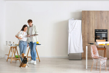 Fototapeta premium Young couple with Beagle dog using mobile phone during repair in their new house