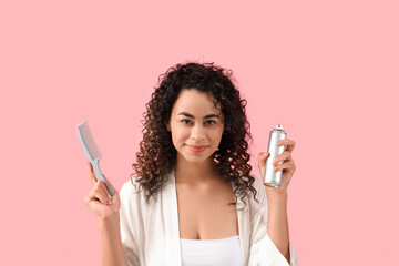Beautiful African-American woman with hair spray and comb on pink background