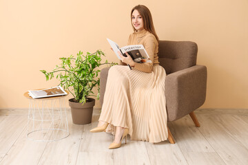 Beautiful woman reading interior magazine in armchair near beige wall