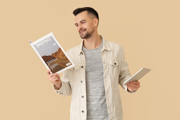 Handsome man with magazine and tablet computer on beige background