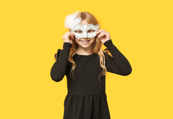Funny little girl wearing carnival mask on yellow background