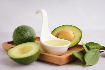 Wooden tray with fresh avocados and spoon of essential oil on white background