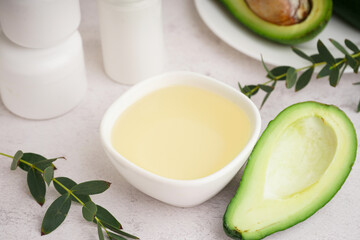 Fresh avocado and bowl with essential oil on white background