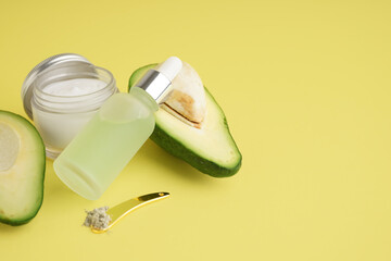 Cosmetic products and fresh avocado on color background