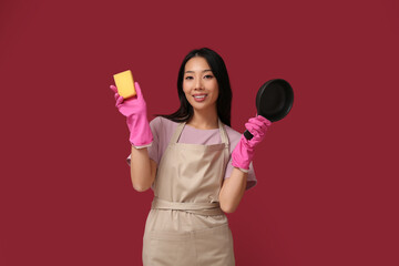 Portrait of young Asian woman with frying pan and sponge on red background