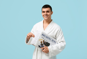 Portrait of handsome young man in bathrobe with newspaper on blue background