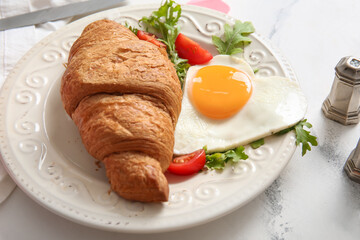 Plate with tasty fried egg, croissant, tomatoes and arugula on light background, closeup