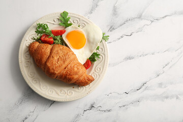 Plate with tasty fried egg, croissant, tomatoes and arugula on light background