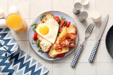 Composition with tasty fried egg, cut croissant, bacon tomatoes and glass of juice on light tile background