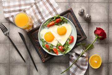 Composition with tasty fried eggs, tomatoes and glass of juice on grey tile background