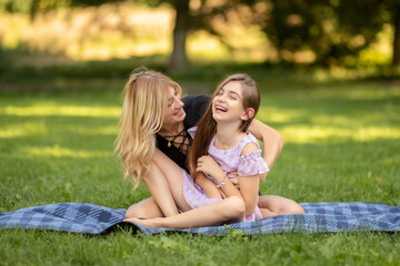 Fototapeta premium Mother and daughter laughing while sitting on a picnic blanket