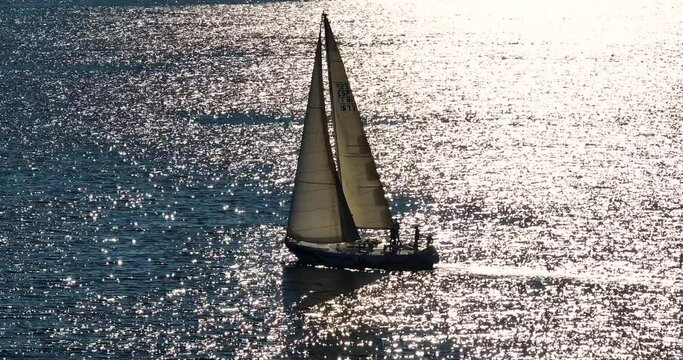 Beautiful sailboat sailing in tropical exotic bay with deep blue sea. Establishing aerial shot of the yacht in the rays of the setting sun. Silhouette of a sailing yacht in the sea shot from a drone