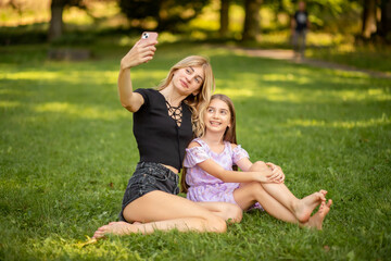 Naklejka na ściany i meble Mother and daughter taking a selfie in the park
