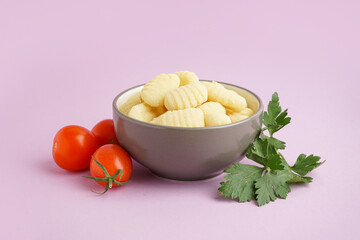 Bowl with tasty gnocchi, tomatoes and parsley on purple background