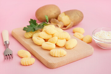Wooden board with tasty gnocchi, grated cheese and parsley on pink background, closeup