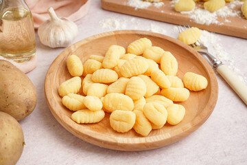 Wooden plate with tasty gnocchi and fork on light background, closeup