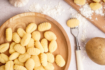 Wooden plate with tasty gnocchi and fork on light background