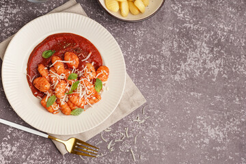 Plate of tasty gnocchi with tomato sauce and cheese on grey background
