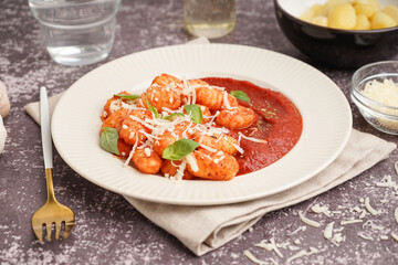 Plate of tasty gnocchi with tomato sauce and cheese on grey background