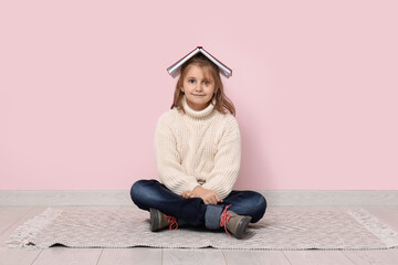 Little girl with book sitting on floor near pink wall