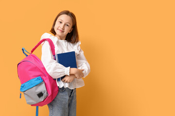 Little schoolgirl with book on yellow background